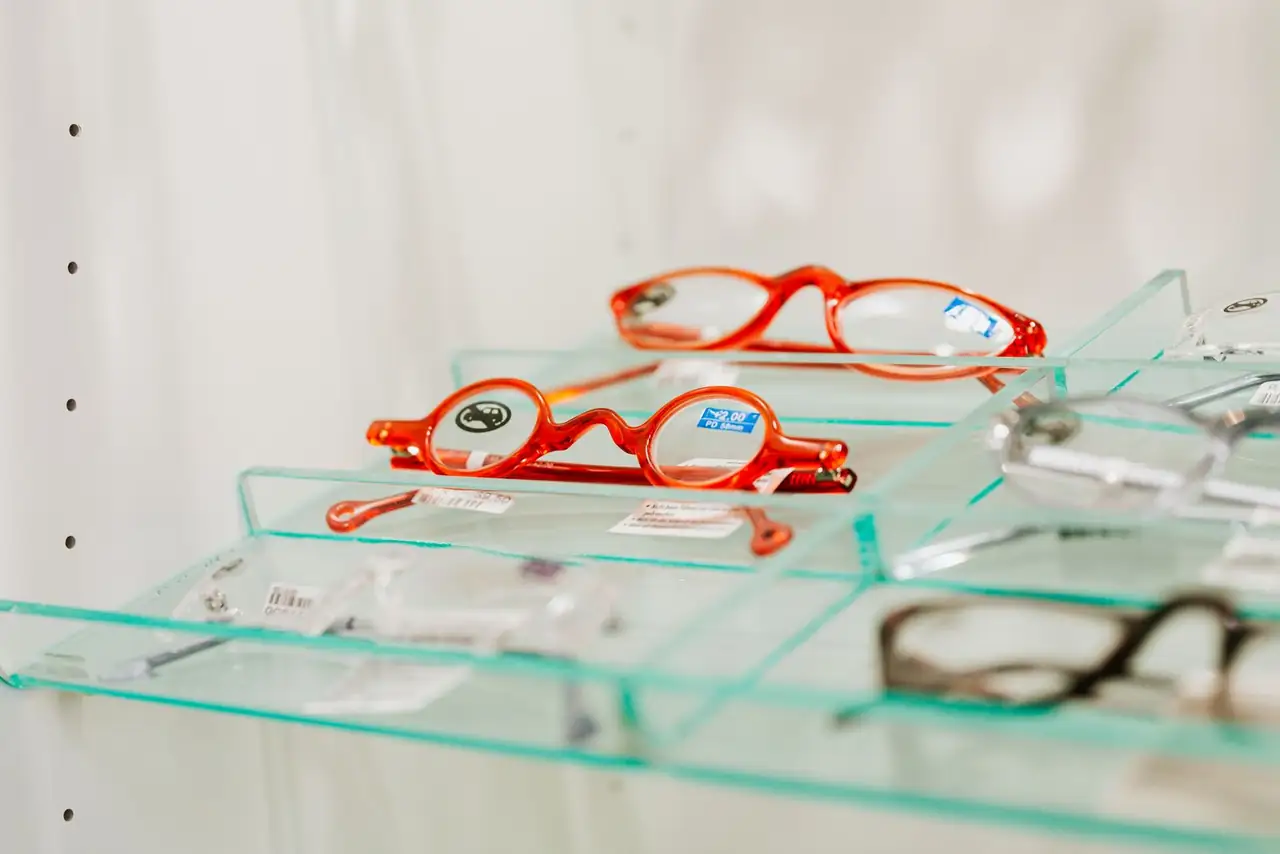 Stylish red eyeglasses displayed on a glass shelf in an eyewear store.