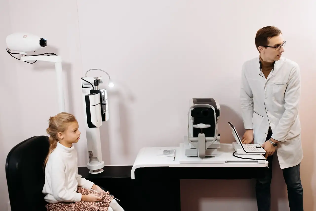 A young girl sits for an eye exam with an optometrist using digital equipment.
